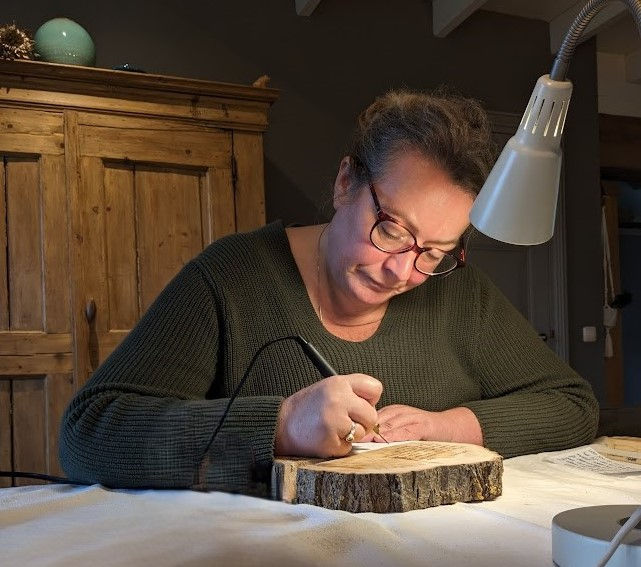 vrouw zit aandachtig een tekst te branden op een boomschijf